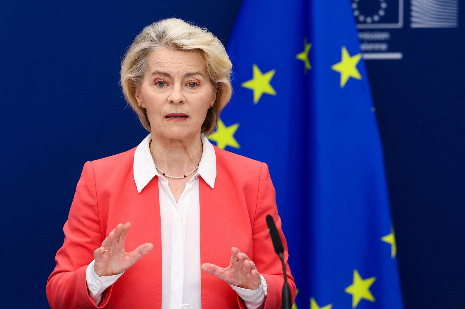 Ursula von der Leyen speaking with an EU flag behind her