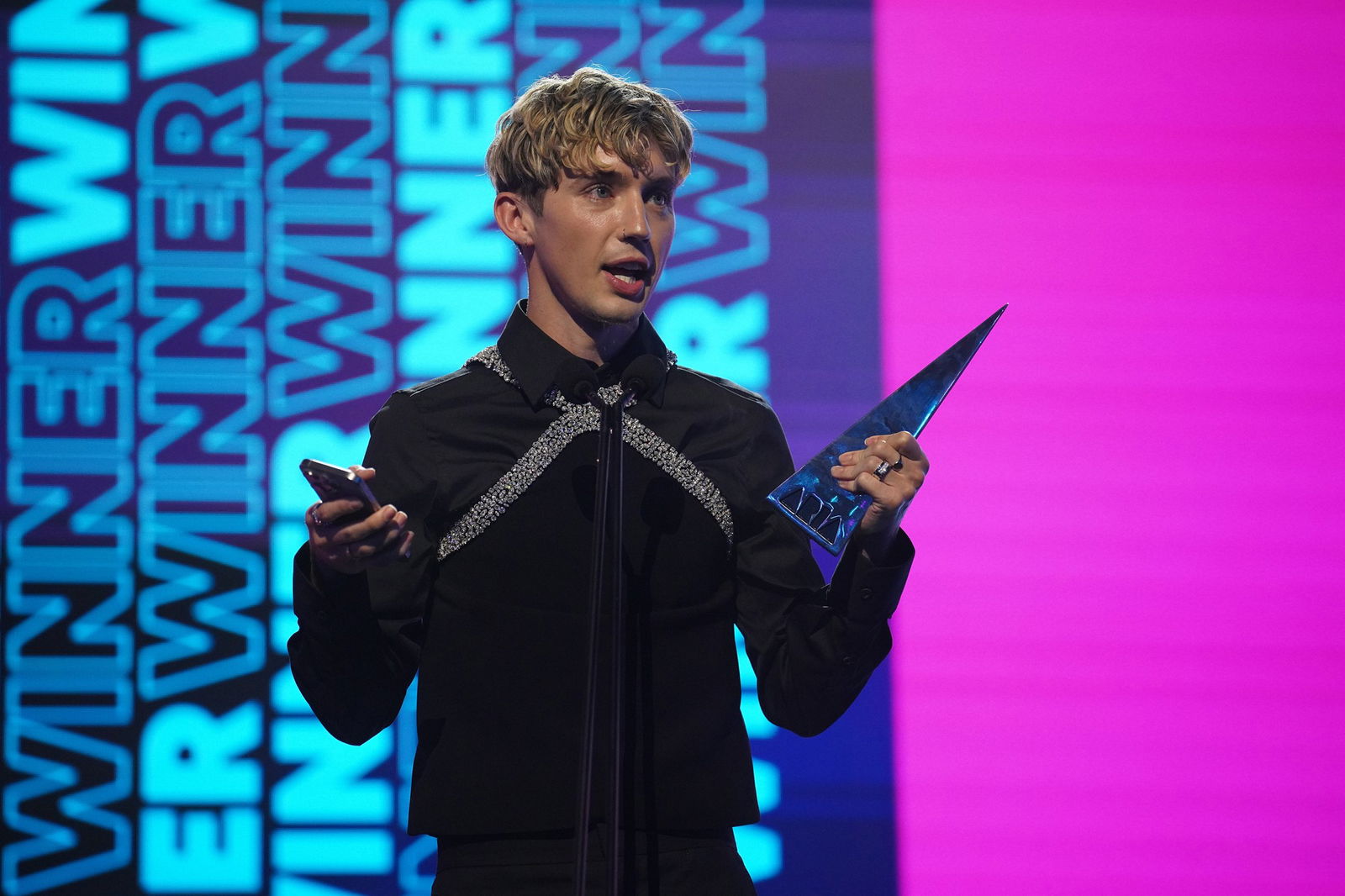 Troye Sivan holding his award in front of a sign reading WINNER