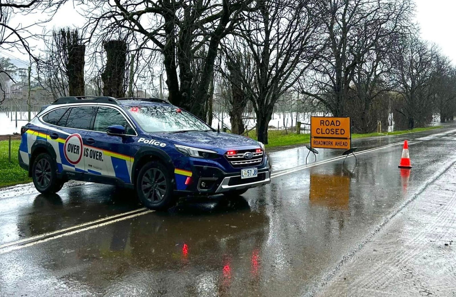 A police car blocking a wet road that's closed.