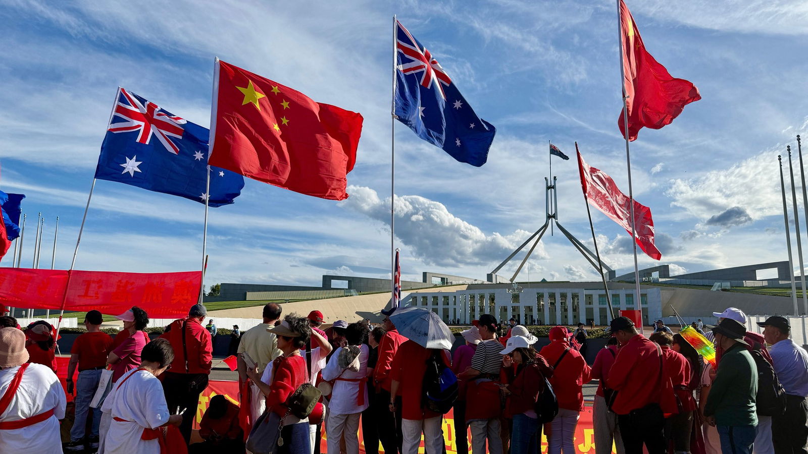 Uma multidão de chineses agita bandeiras chinesas e australianas em frente ao parlamento.