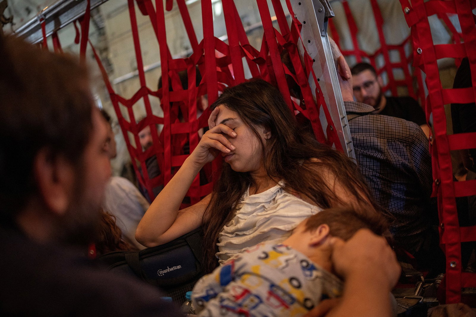 a woman covers her face with her hand as she rests in a cargo hold with red straps everywhere supporting people