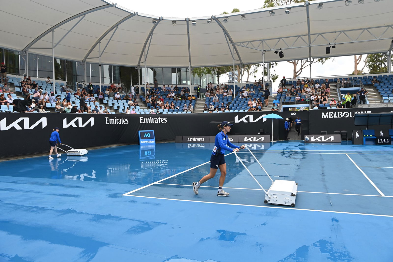 A tennis court with ball kids moping up the rain