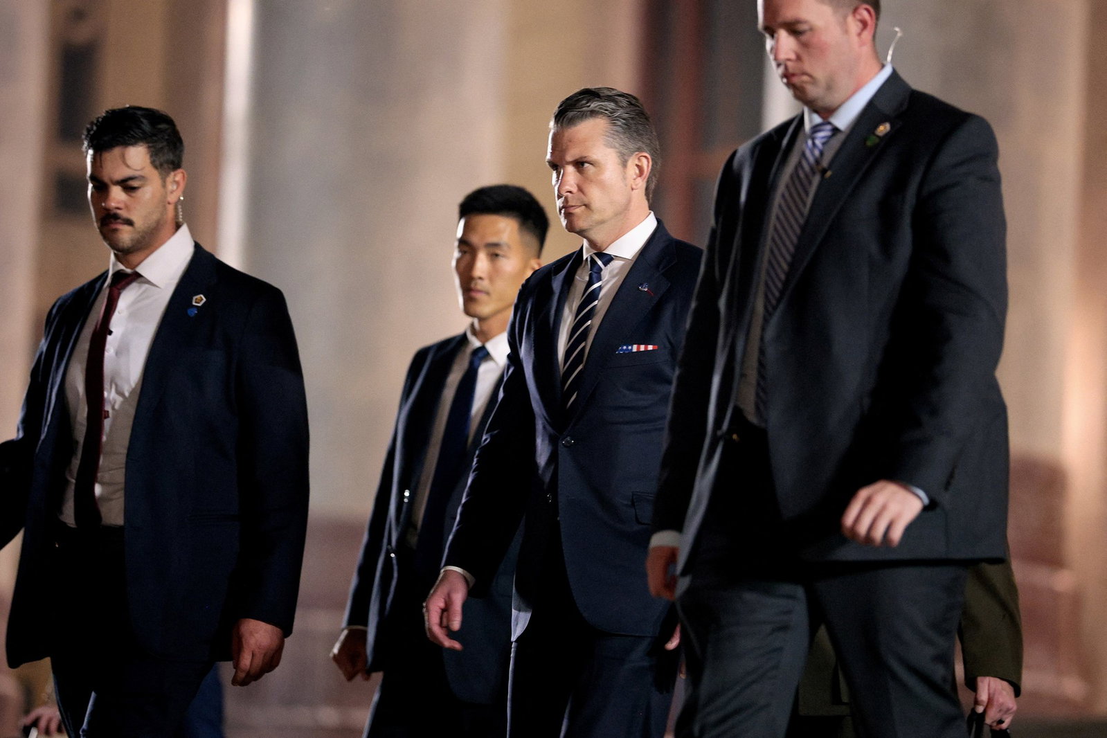 Four men wearing suits exit a building.