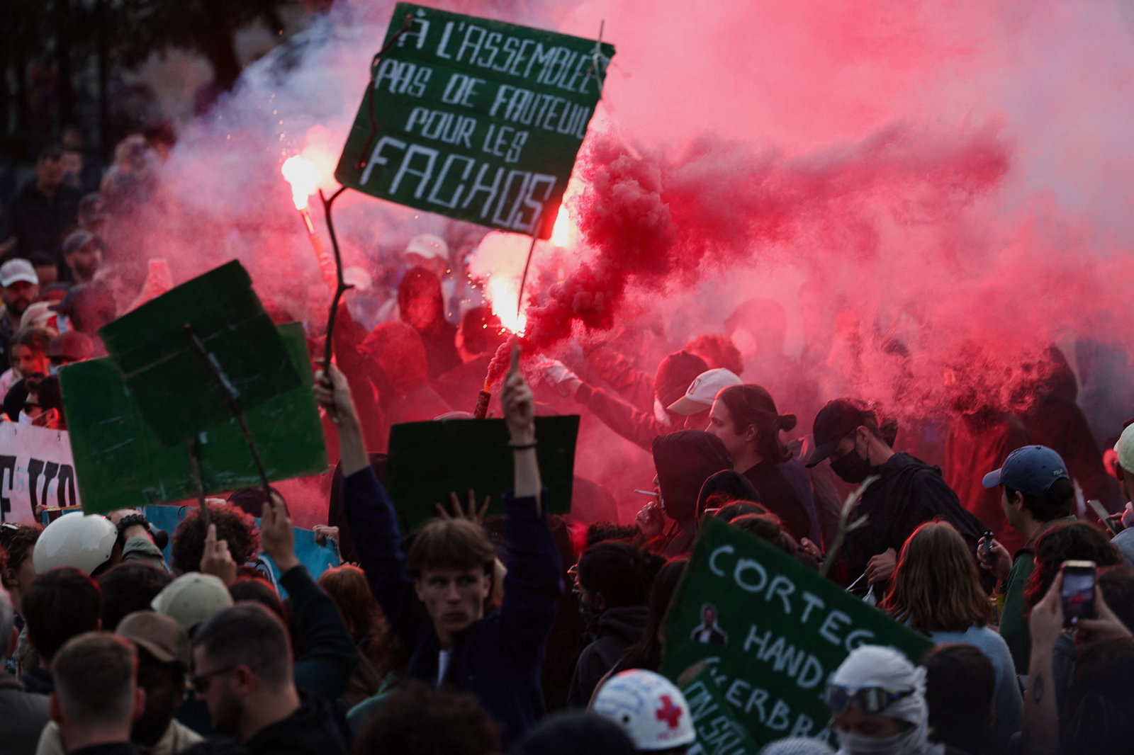 Red flares lit up amongst a crowd holding signs