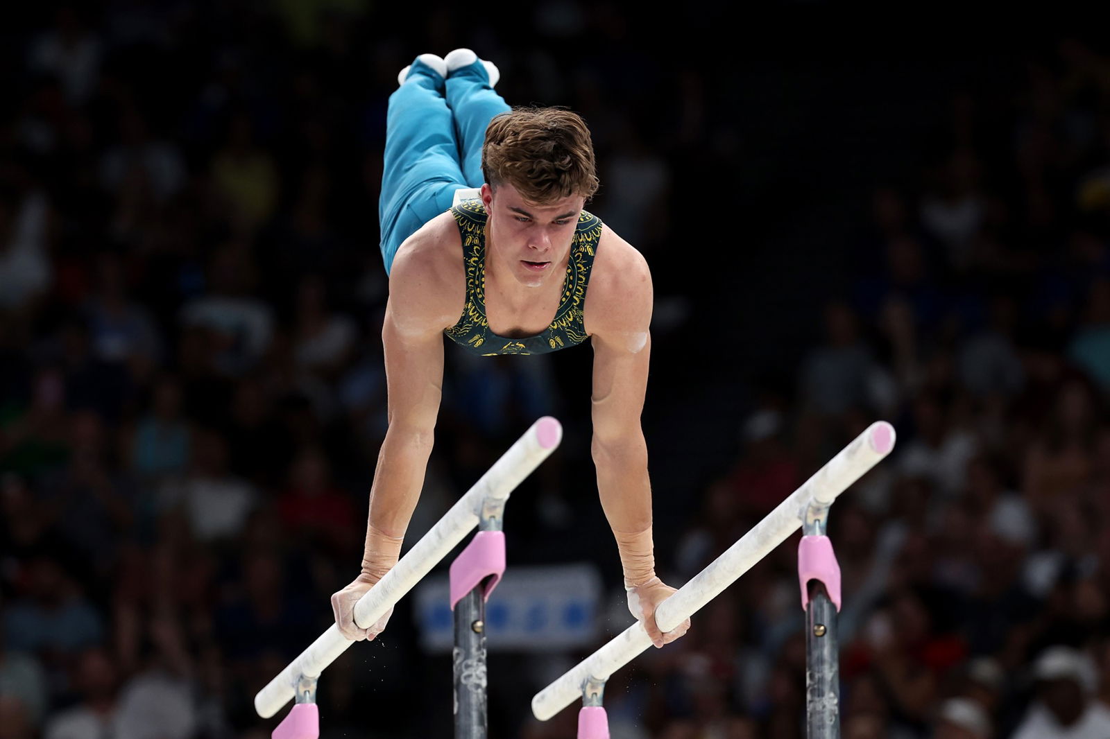  Jesse Moore has two hands on the parallel bars and his legs in the air behind him.