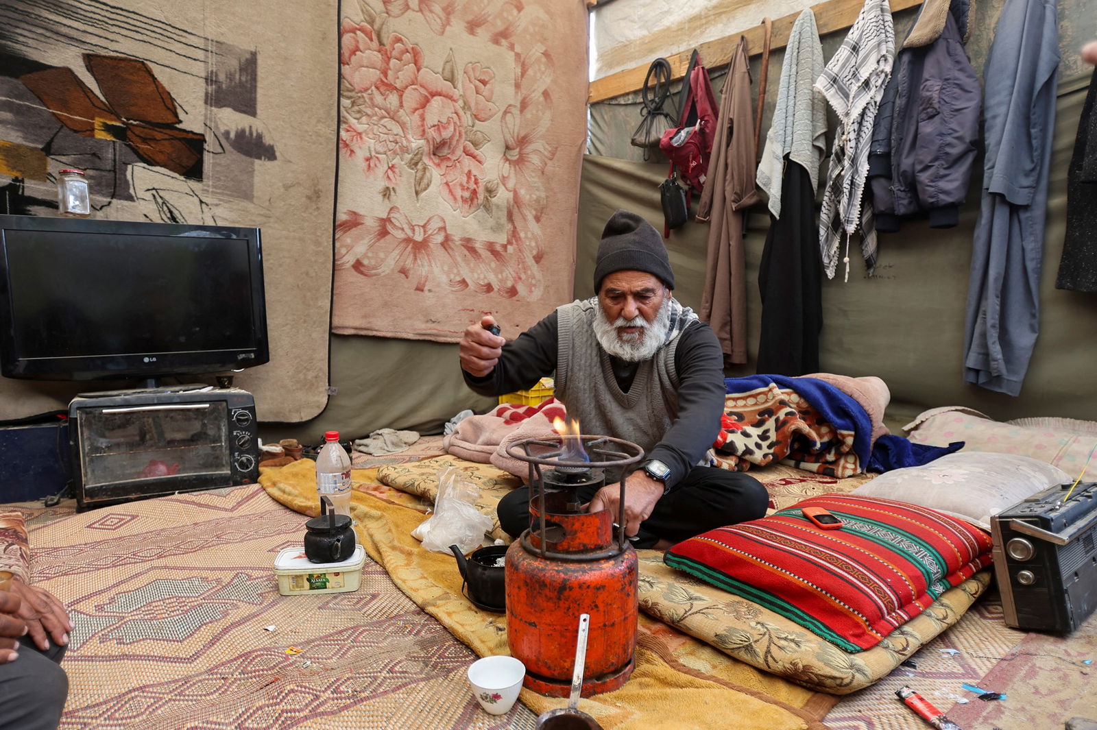 A man sits on a carpet and blankets on the ground. 