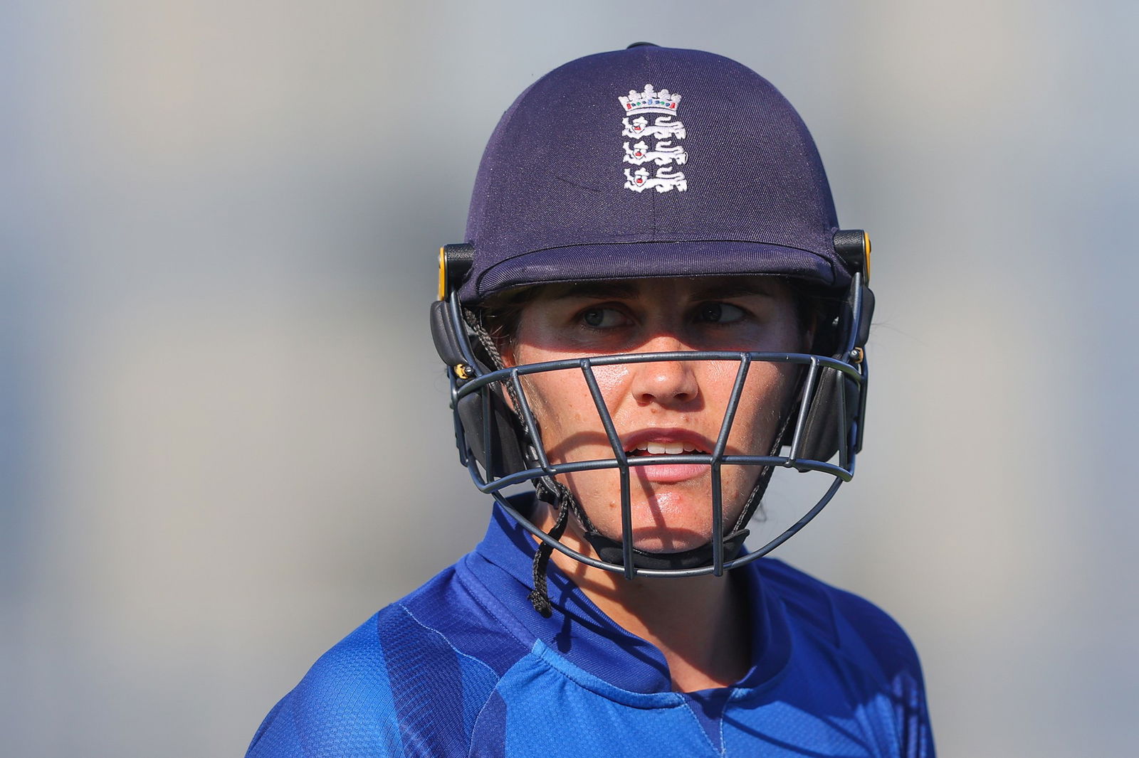 A woman in a blue top and blue, England cricket helmet stares at camera