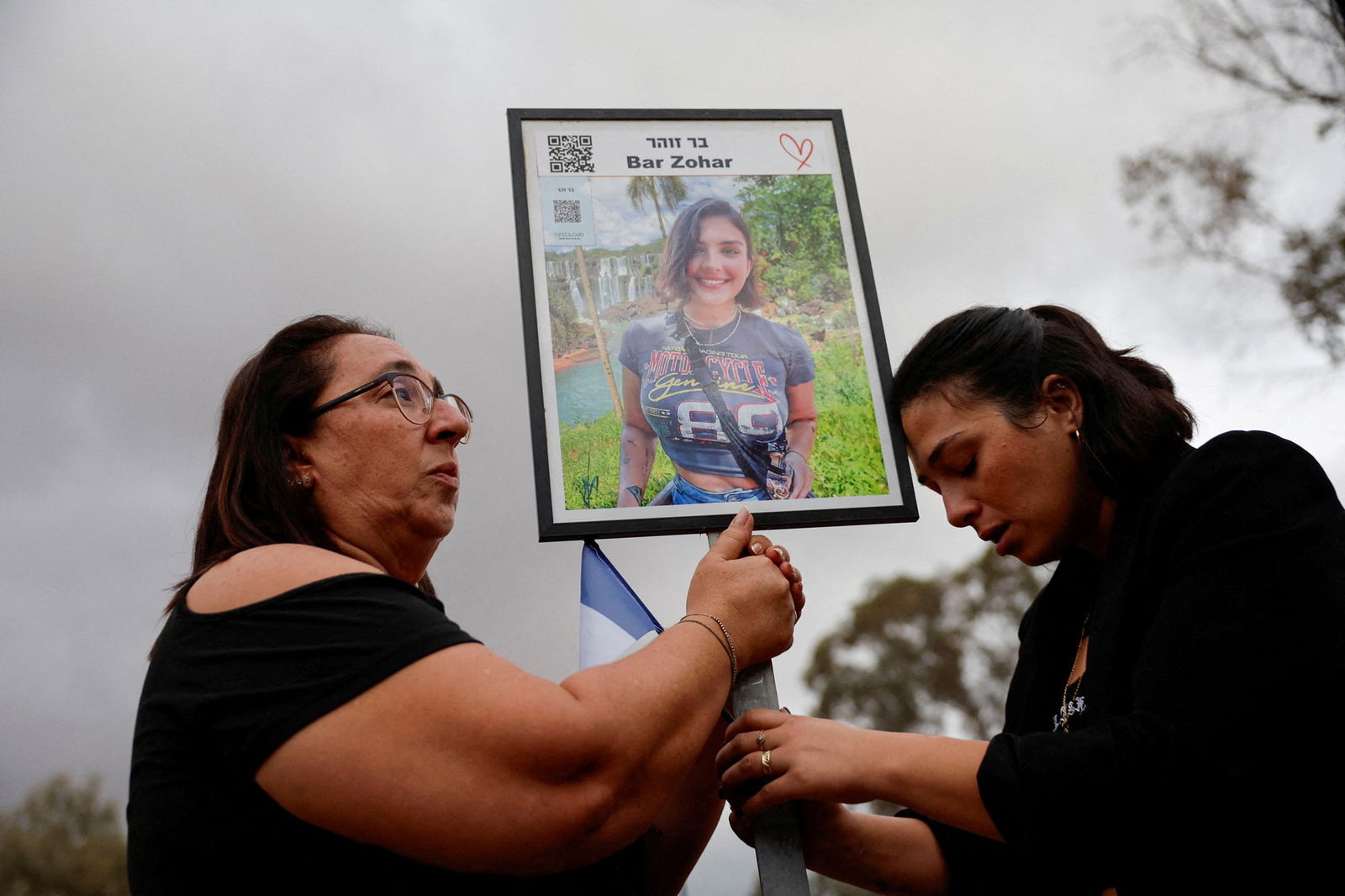 Two women hold a poster depicting another woman