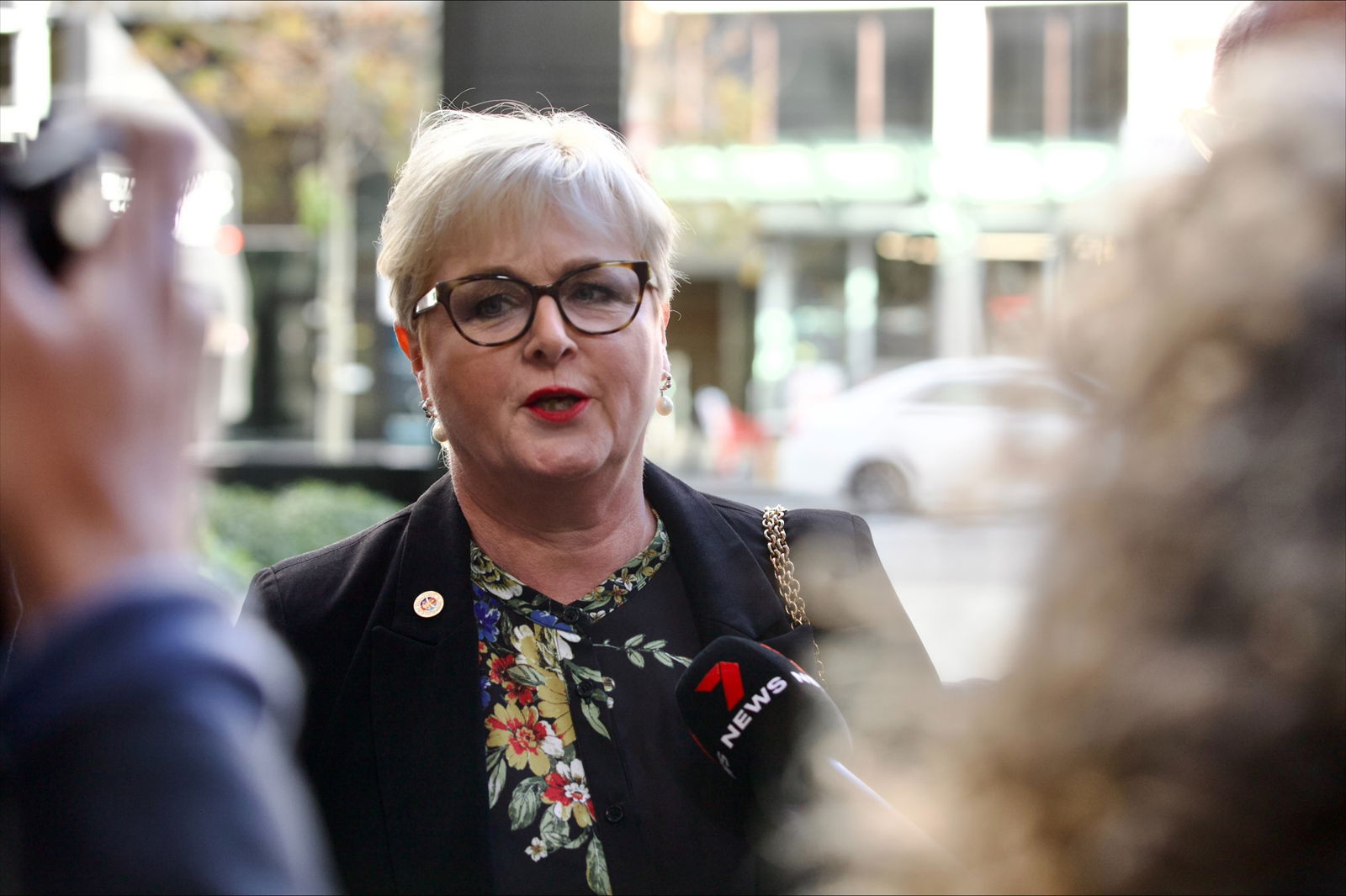 A woman wearing glasses is questioned by reporters.