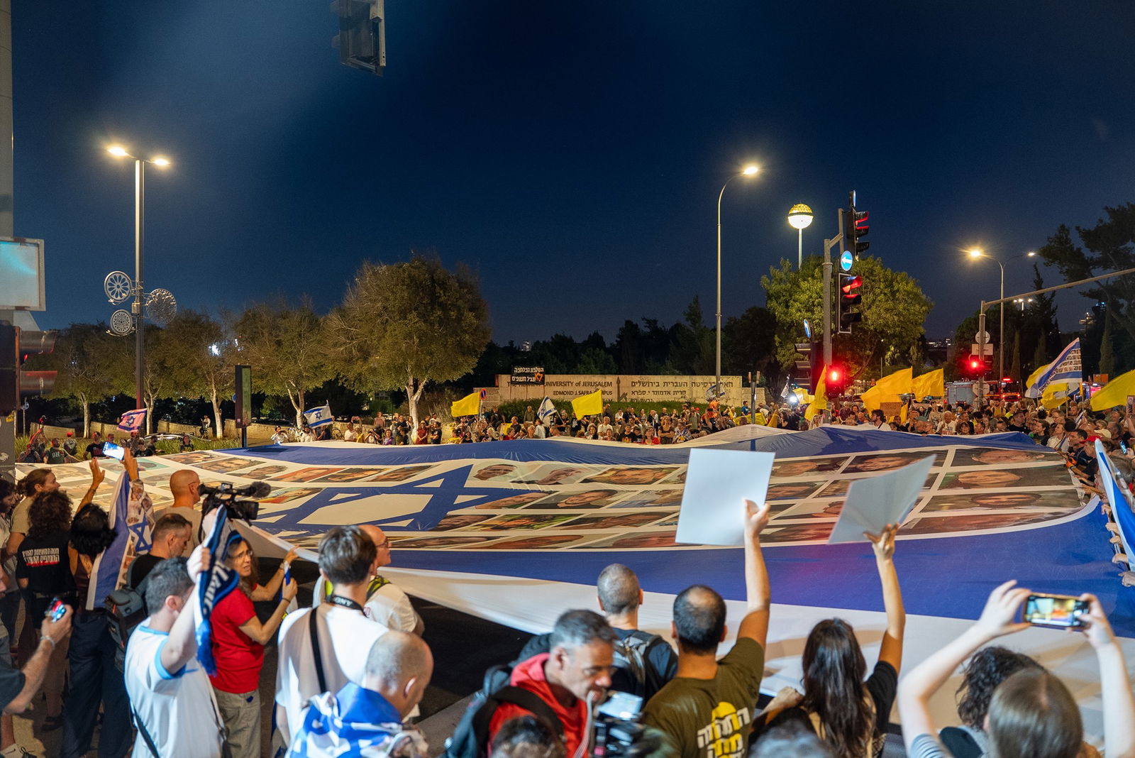 A large Israeli flag is carried by protesters.