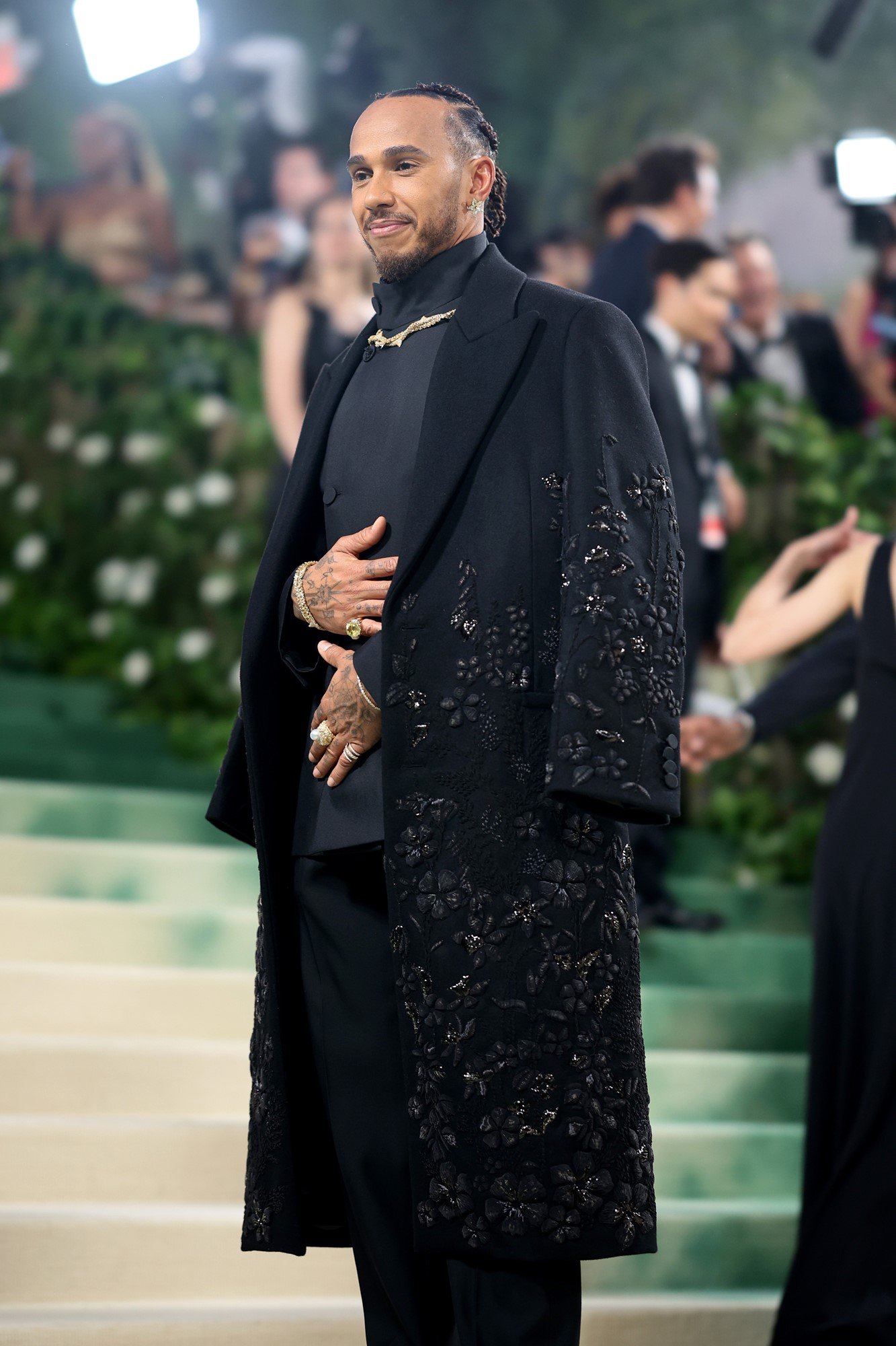 Hamilton poses on the steps in a black embroided coat.