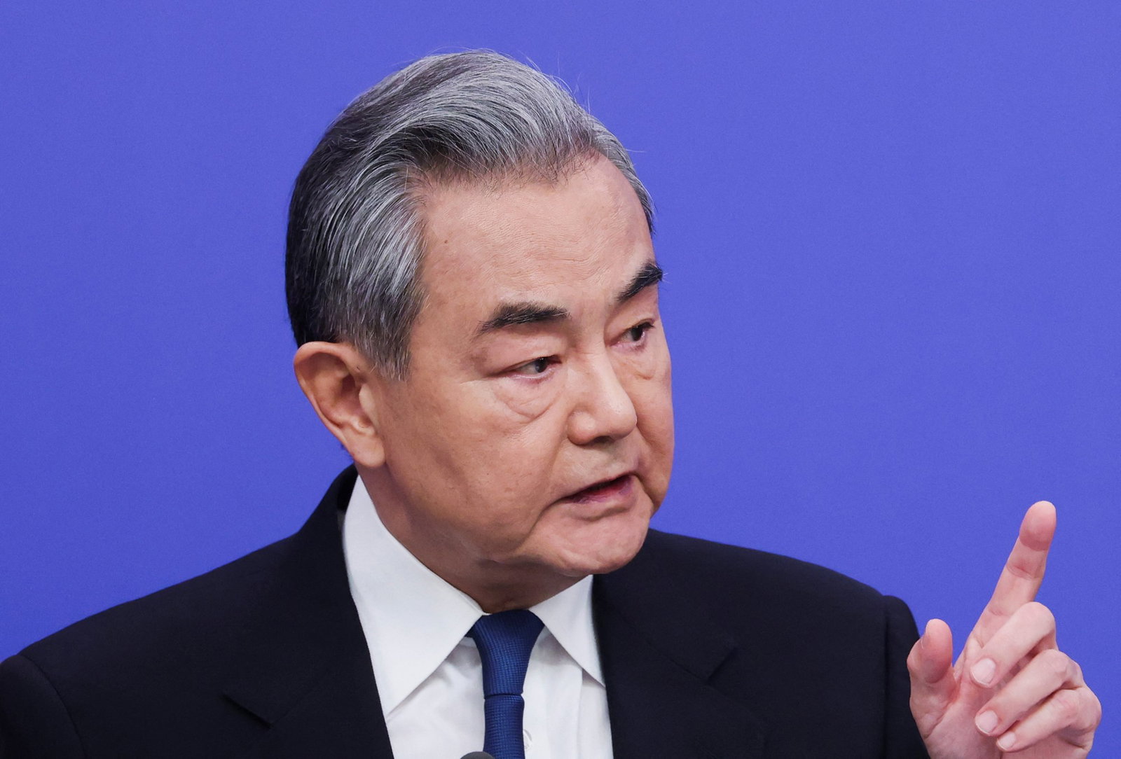 Yi raises a finger and looks to his side as he speaks