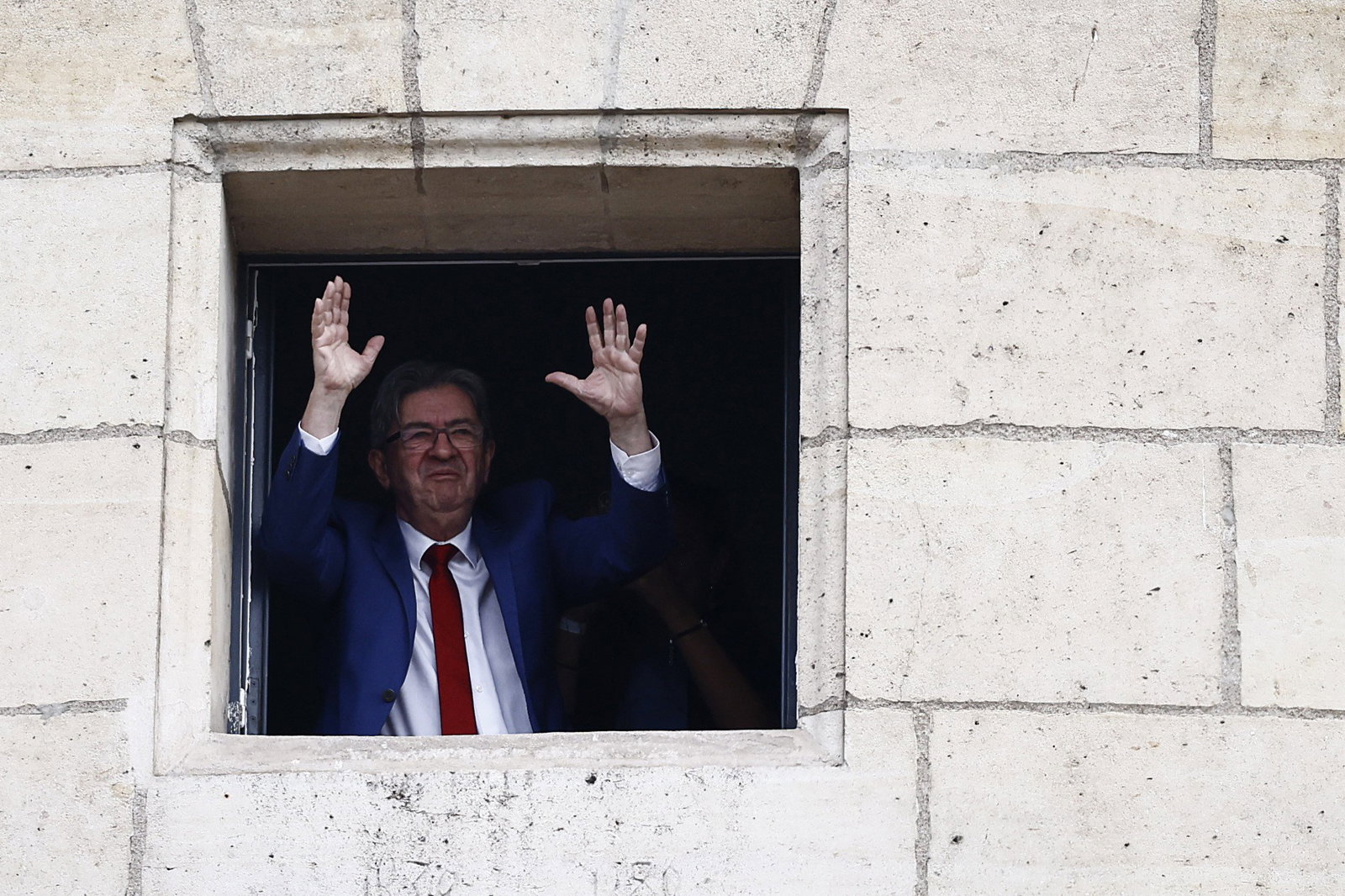 A man waves out a stone window 