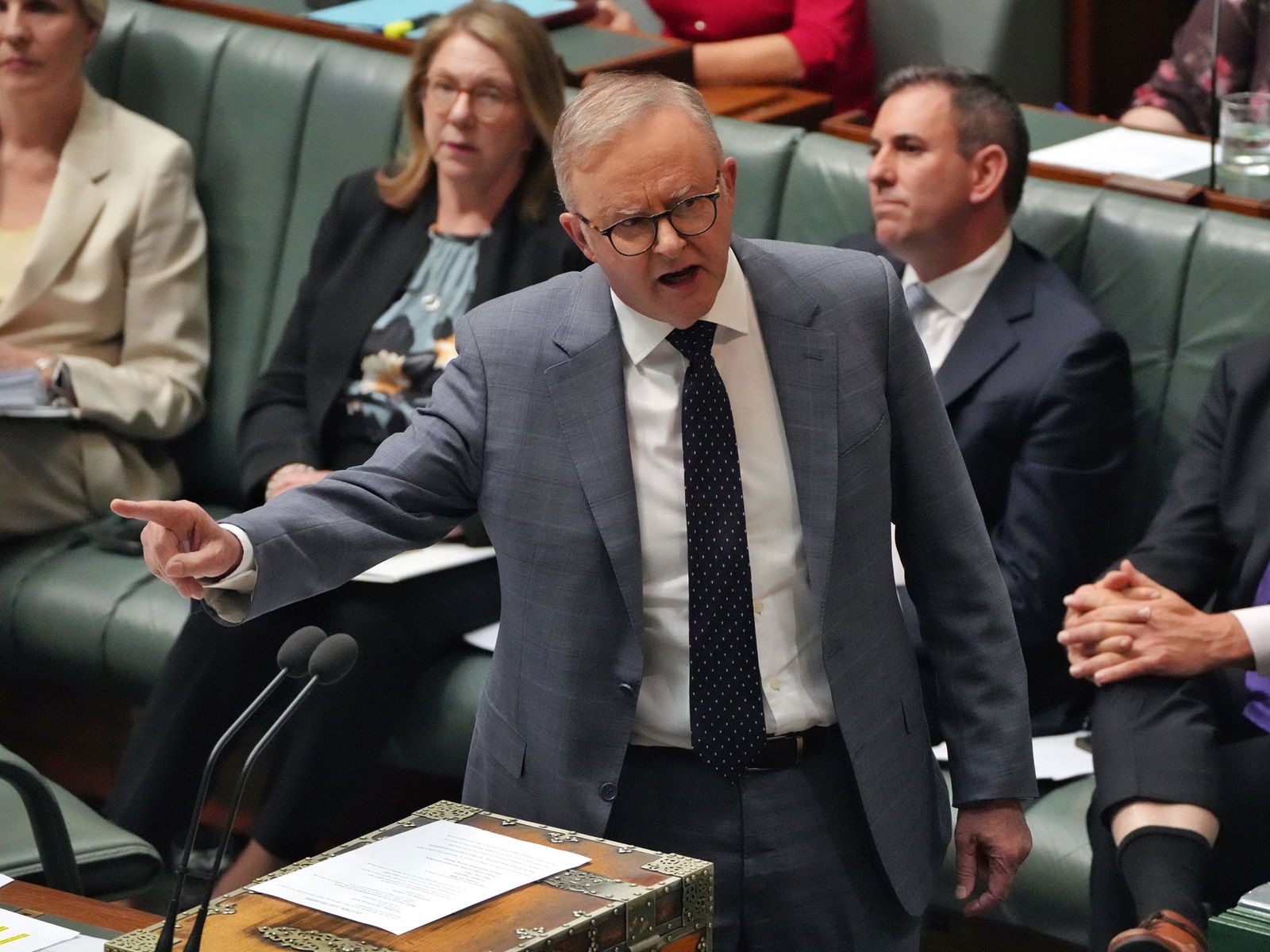 Man in a grey suit points his finger across a table