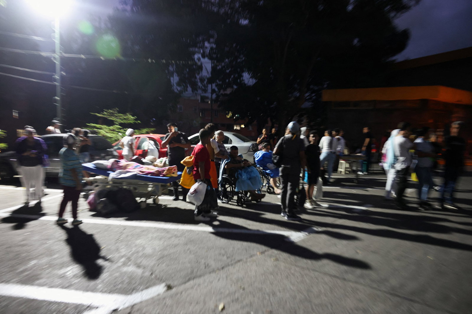 Patients, some in hospital beds, wait outside a hospital at night.