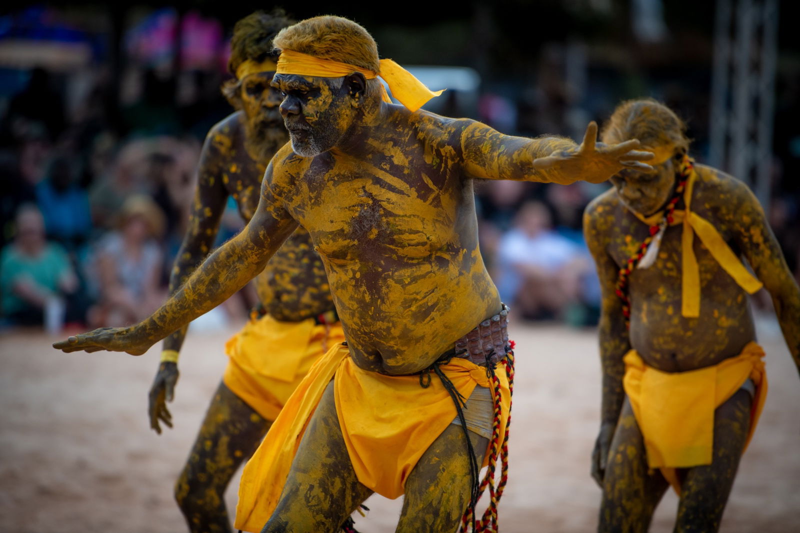 Indigenous men dance on a sandy space.