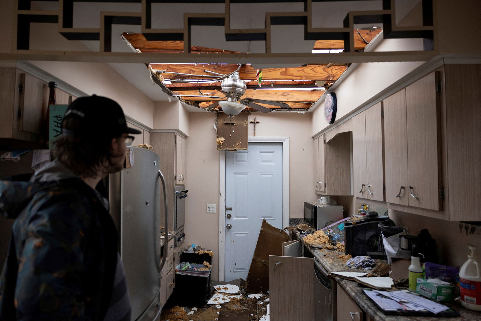 A man looks at destroyed home, roof exposed and debris covers kitchen 