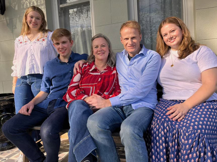 Richard Scolyer, vestido con una camisa azul, está sentado sonriendo con su hija, su hijo y su esposa a un lado y su otra hija a la derecha.