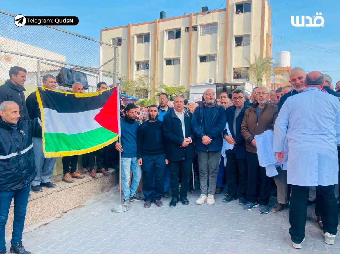 A large group of people standing outside, including some holding a Palestinian flag.