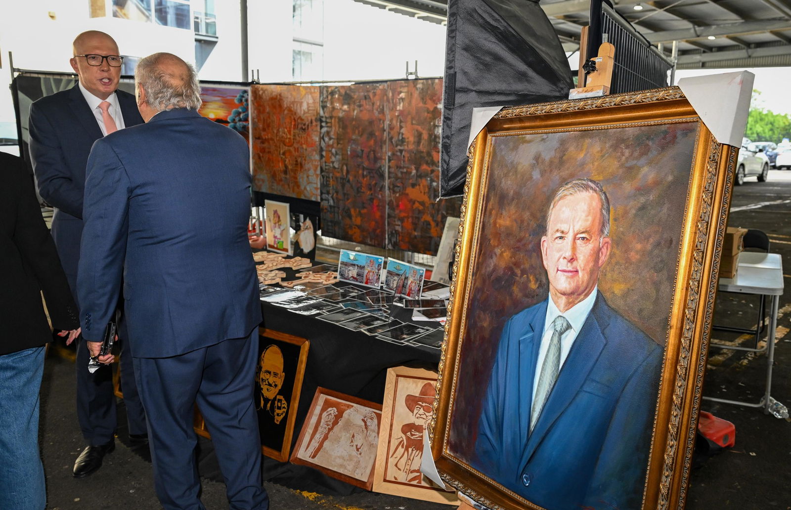 Peter Dutton speaks with a man beside a large painted portrait of Anthony Albanese.