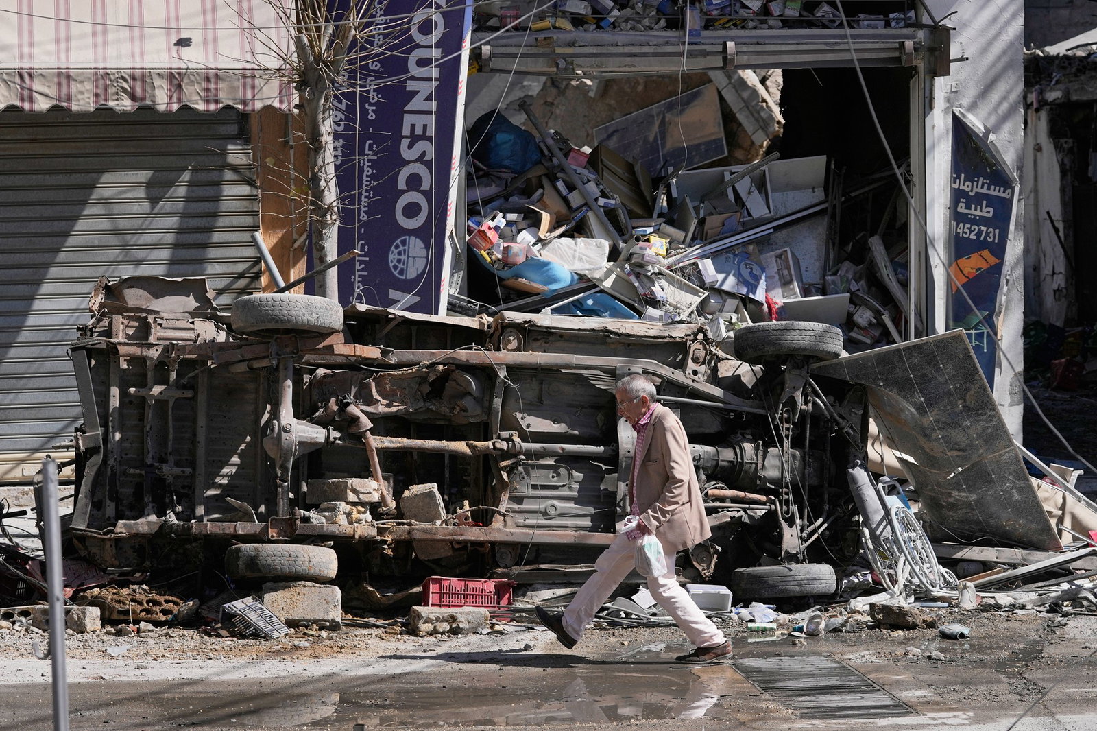 A man passes by a destroyed car and shop on a commercial street that was hit by Israeli airstrikes in Nabatiyeh town, south Lebanon.