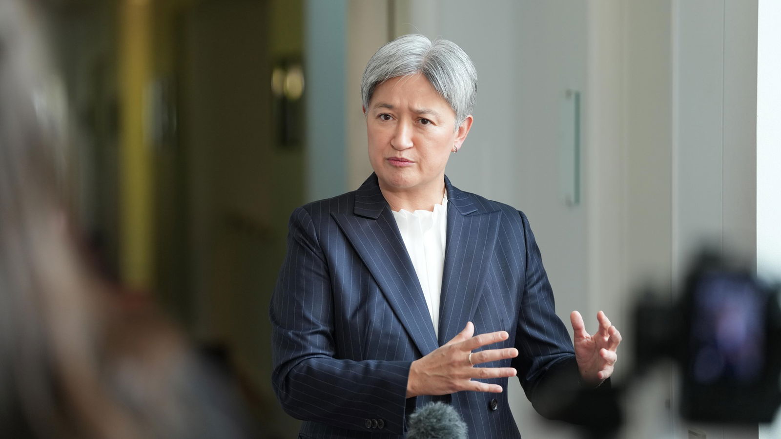 A Southeast Asian woman with mostly white-grey hair speaks in a suit