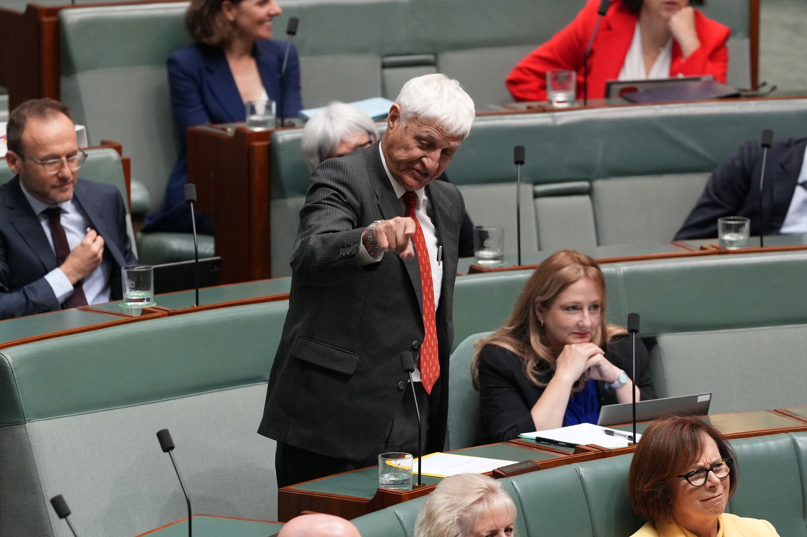 Man in black suit and red tie stands up 