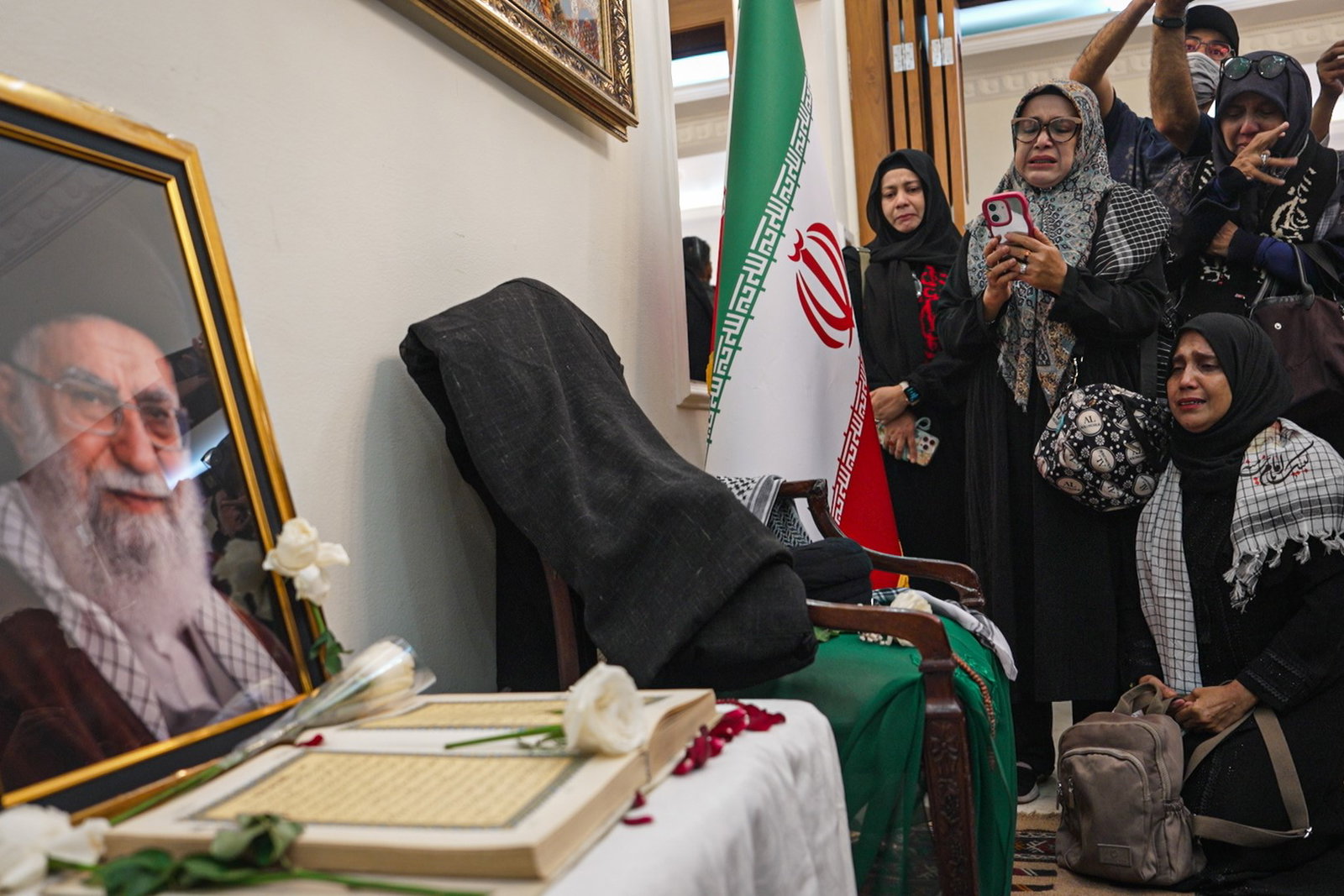 people crying next to a flag of Iran and looking at a picture of the Ayatollah