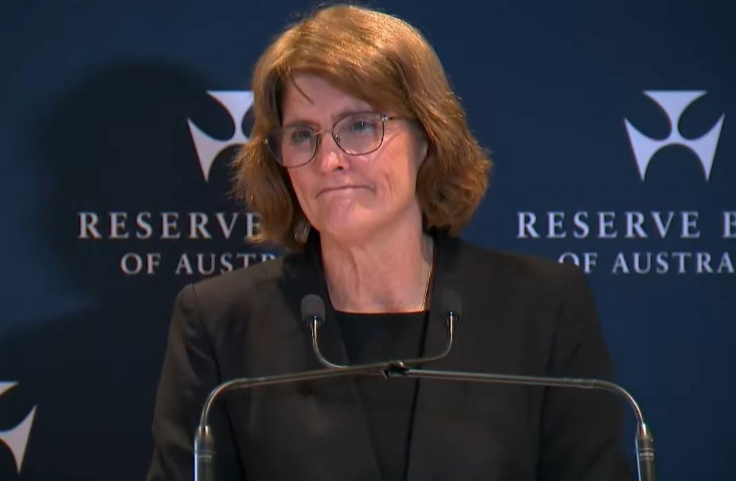 A woman wearing glasses standing in front of two microphones.