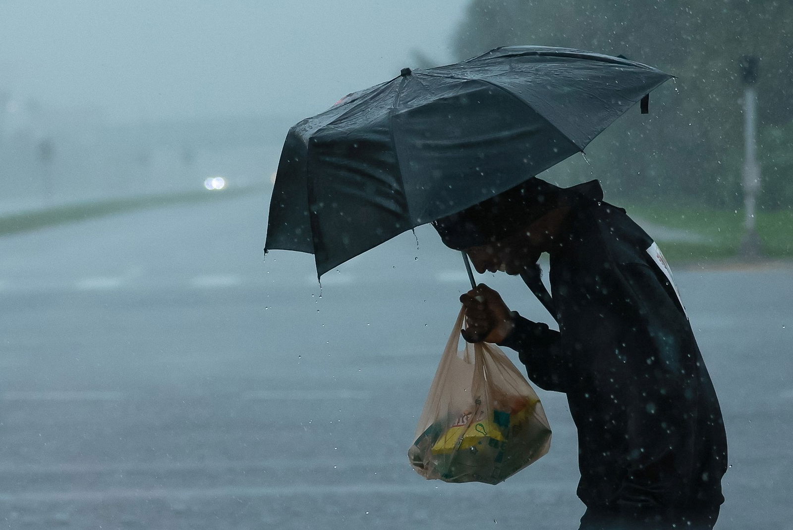 A person holds an umbrella and yellow plastic bag in rain