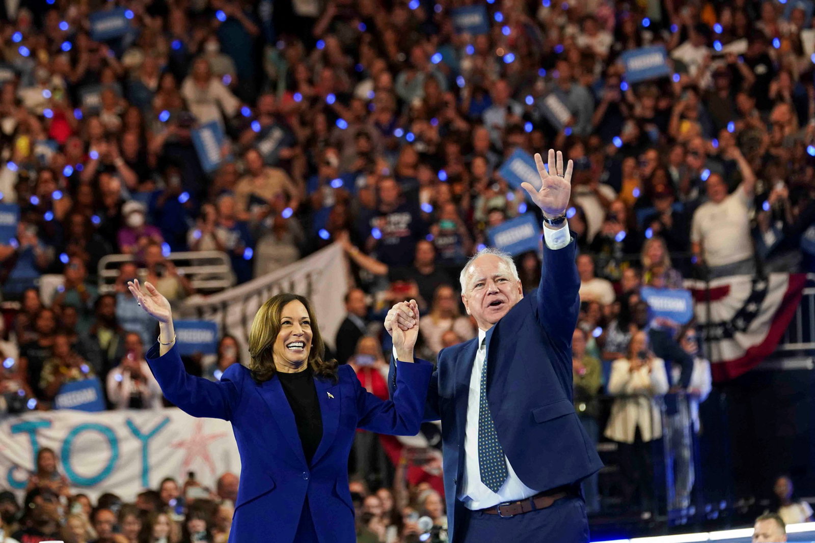 Kamala Harris and Tim Walz wave on stage at a campaign rally